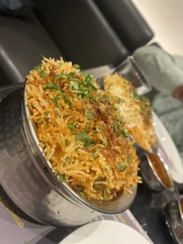 Beef biryani heaped high in a steel serving pot, garnished with fresh herbs