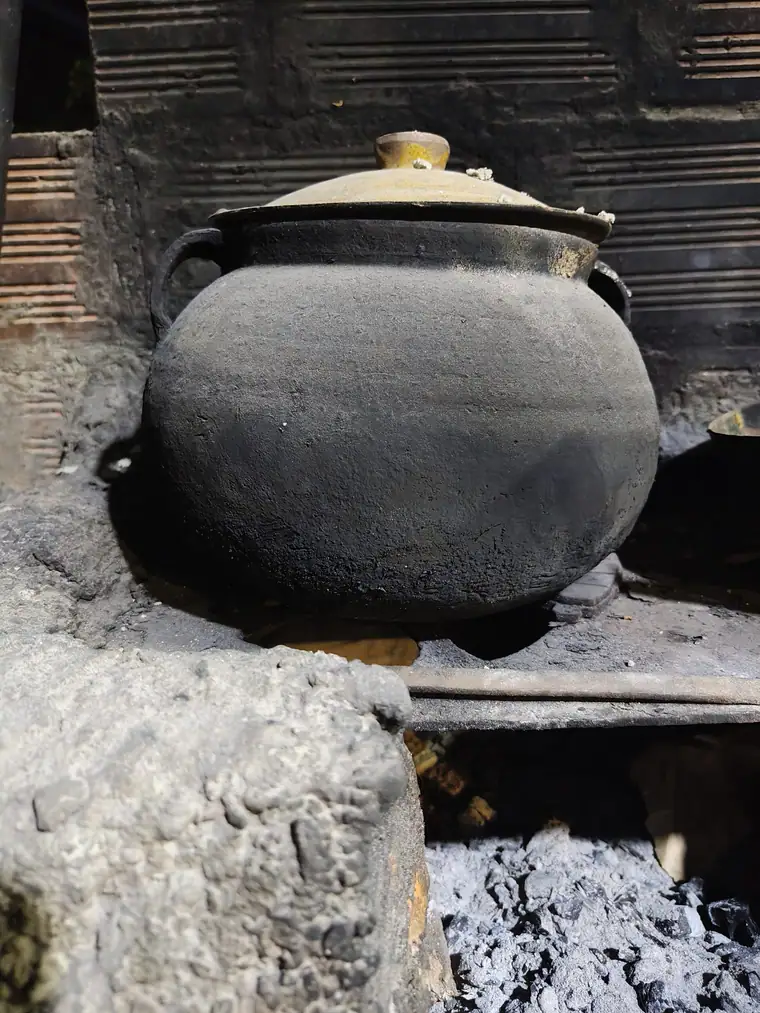 A heavy black cooking pot sitting over a wood fire