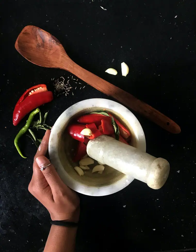 Fresh red chillies and garlic being pounded in a stone mortar