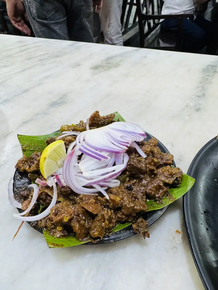 Spiced beef served on a banana leaf with raw onion rings and lime
